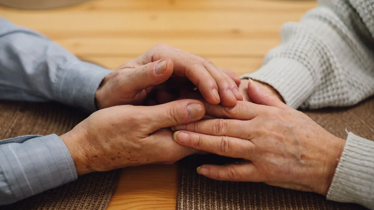 Two older people holding hands across a wooden table in support